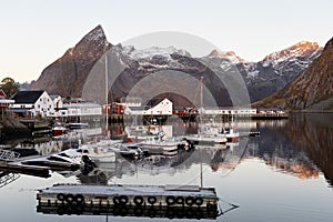 A small pier with boats at Hamnøy with historic buildings and snowclad mountains in the background, Lofoten, Norway