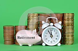 The small piggy bank with pile of coins and white retro alarm clock on green background.