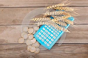 Small pile of ripe wheA calculator with ripe wheat ears on it and a pile of euro coins next to itat ears on calculator