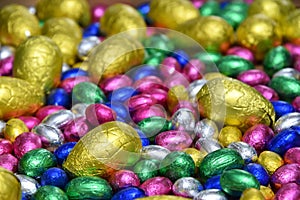 Small pink, blue, green and silver foil wrapped chocolate easter eggs with larger yellow eggs, as a background.
