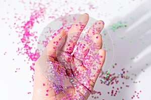 Small pink heart shape sequins on young female hand on white background. Valentine's day concept. Female hand with pink heart