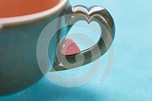 Small pink red heart shape sugar candy on coffee cup handle on mint blue background. Valentines Mothers Day charity concept
