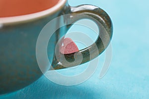 Small Pink Red Heart Shape Sugar Candy on the Handle of Coffee Tea Cup on Light Blue Background. Valentines photo