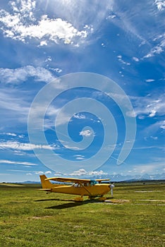 Small plane standing on a grass field against Tatra Mountains and blue cloudy sky