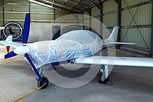 small plane with a three-bladed propeller of private aviation stands covered with a cover in a bright hangar