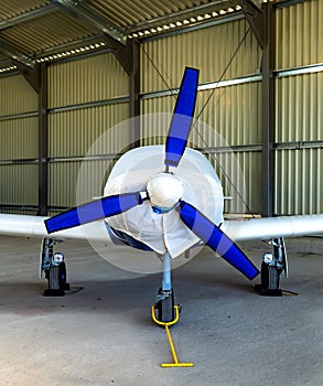 small plane with a three-bladed propeller of private aviation stands covered with a cover in a bright hangar