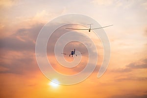 A small plane towing a glider toward the setting sun