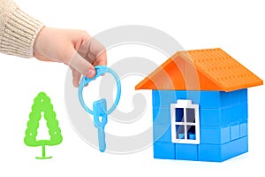 a small plastic house with a hand holding out the keys on a white insulated background. the concept of selling, buying, or