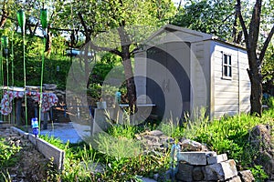 Small plastic tool storage shed placed in spring terrace garden, with round table in front