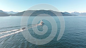 A small pleasure craft towing a dingy with Howe Sound and the mountains in the background on a sunny day. 24FPS 4K.