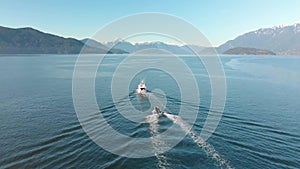 A small pleasure craft towing a dingy with Howe Sound and the mountains in the background on a sunny day. 24FPS 4K.