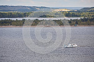 Small pleasure karabl floating on the river against the background of the coast with trees and mountains