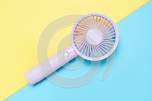 Small portable mini fans on blue and yellow background close-up.