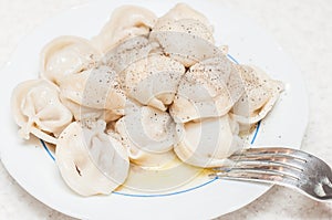 A small portion of freshly cooked dumplings with butter sprinkled with pepper on a white plate with a fork