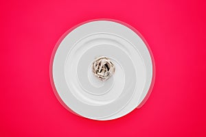 Small portion of tagliatelle pasta on round white plate on pink tablecloth.