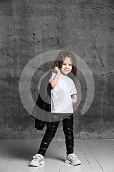 Small positive girl in black and white rock style clothing and white sneakers standing and posing over grey concrete background