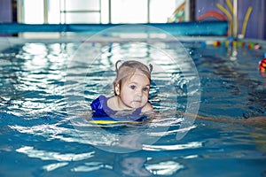 Small preschooler child learns to swim with board in pool. Swimming lesson. Active child plays in water