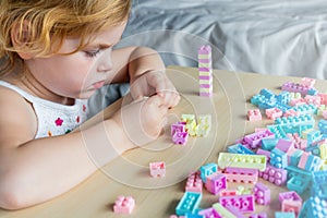 Small preschooler girl playing with colorful toy building blocks, sitting at the table