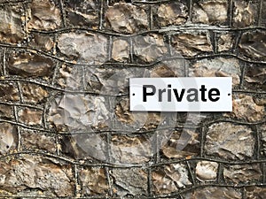 A small private sign black text on a white background attached to a rock wall empty space to the left