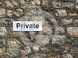 A small private sign black text on a white background attached to a rock wall empty space to the right