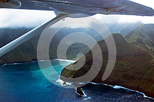 Small prop airplane flies over Maui`s tall sea cliffs