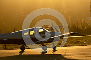 A small propeller plane rolling down the runway in backlight under a yellow sunset sun