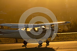 A small propeller plane rolling down the runway in backlight under a yellow sunset sun