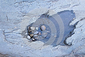 Small puddle with pebbles in grey rock formation