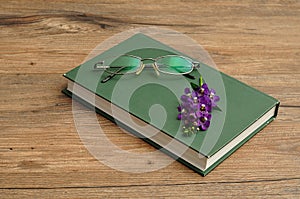 Small purple flowers with a hardcover storybook and spectacles