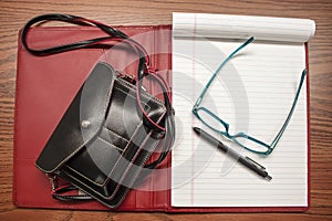 Small purse and notebook and pen and reading glasses flat lay - red and black leather with turquoise glasses and lined notebook pa