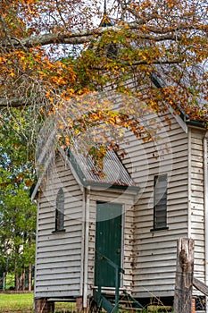 Small quaint disused rural white weatherboard church front entrance surrounded by autumnal trees