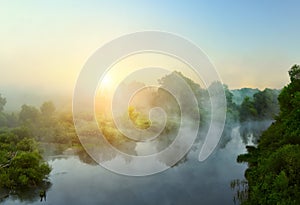 Small quiet river at dawn, green overgrown coast meandering river, fog, mist over the water.