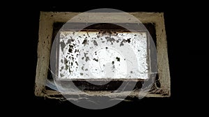 A small rectangular dirty and dusty web window in a large basement. White light penetrates the dark basement photo