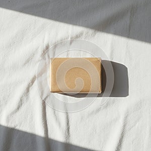 A small rectangular package wrapped in light brown paper lies on a white fabric surface