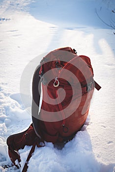 Small red backpack stands on the white snow