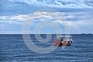 Small red boat on blue sea surface on cloudy day
