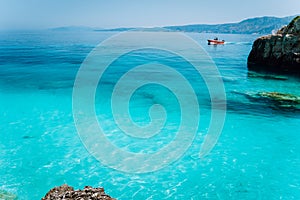 Small red boat floating on clear blue sea water. Summer beach vacation relaxation concept
