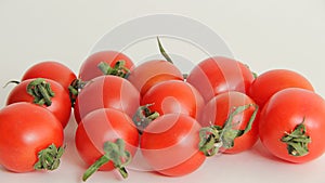 Small red Cheri tomatoes with green tails lie scattered on a white background