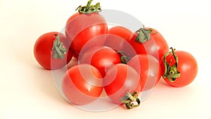 Small red Cheri tomatoes with green tails lie scattered on a white background close up