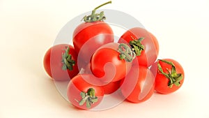 Small red Cheri tomatoes with green tails lie scattered on a white background close up