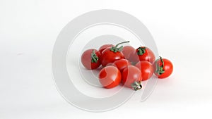 Small red Cheri tomatoes with green tails lie scattered on a white background close up