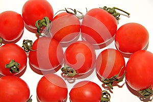Small red Cheri tomatoes with green tails lie scattered on a white backgroundred tomatoes with green tails in a glass vase on a wh photo