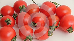 Small red cherry tomatoes with green tails lie scattered on a white background