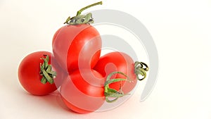 Small red Cherry tomatoes with green tails lie scattered on a white background close uy