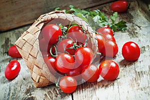 Small red cherry tomatoes spill out of a wicker basket on an old