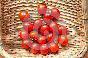 Small red cherry tomatoes spill out of a wicker basket on an old wooden table in rustic style, selective focus