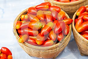 Small red cherry tomatoes spill out of wicker basket on an old wooden table in rustic style