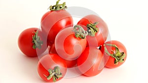 Small red Chery tomatoes with green tails lie scattered on a white background close uy