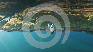 A small red cottage and a boat house on the fjord shore