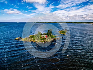 A small red cottage on an island in the blue sea on a summer day. Finland. View from above.